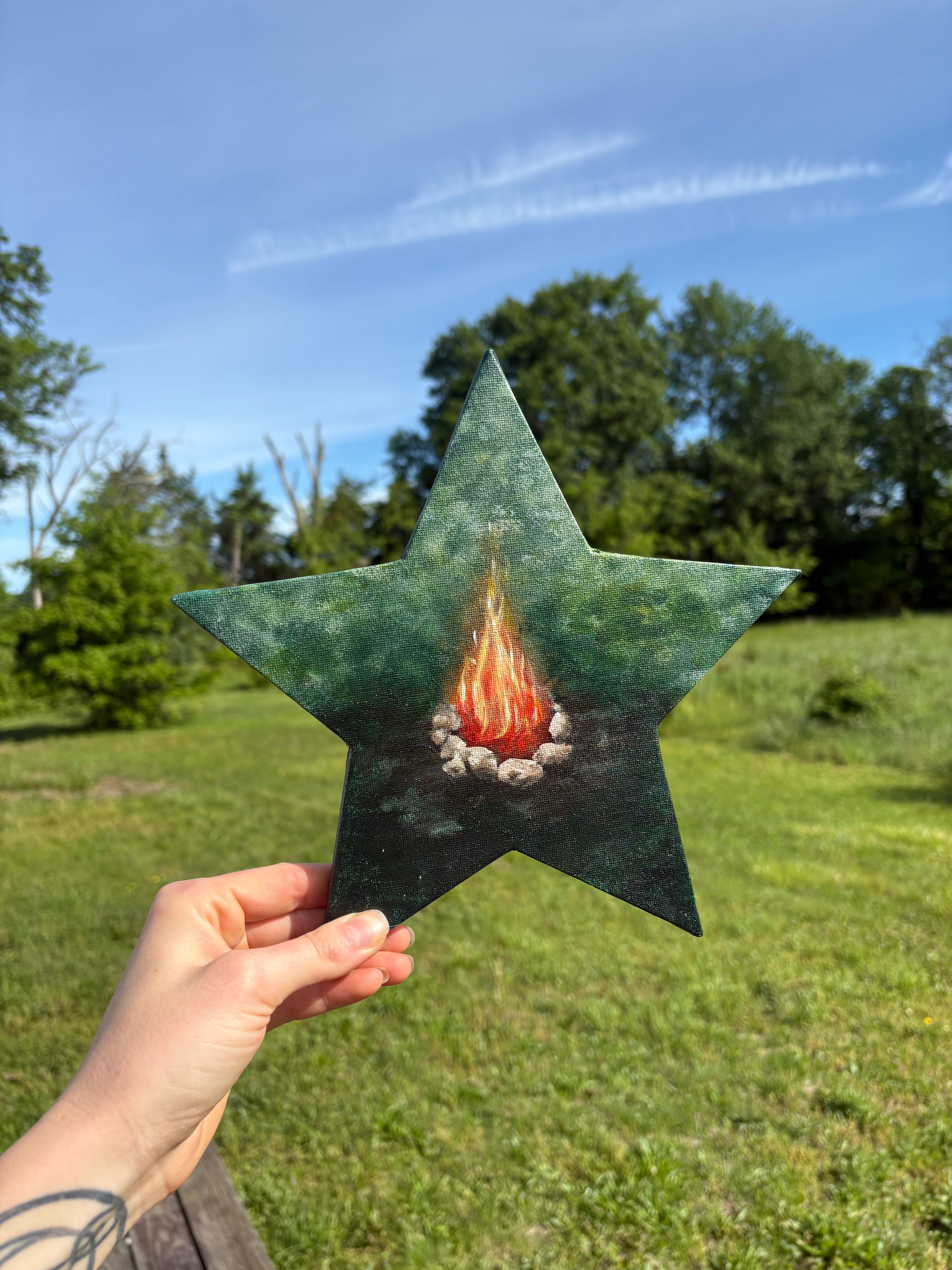 Person holding a star-shaped paper with a rocket illustration outdoors, green grass and trees in background.