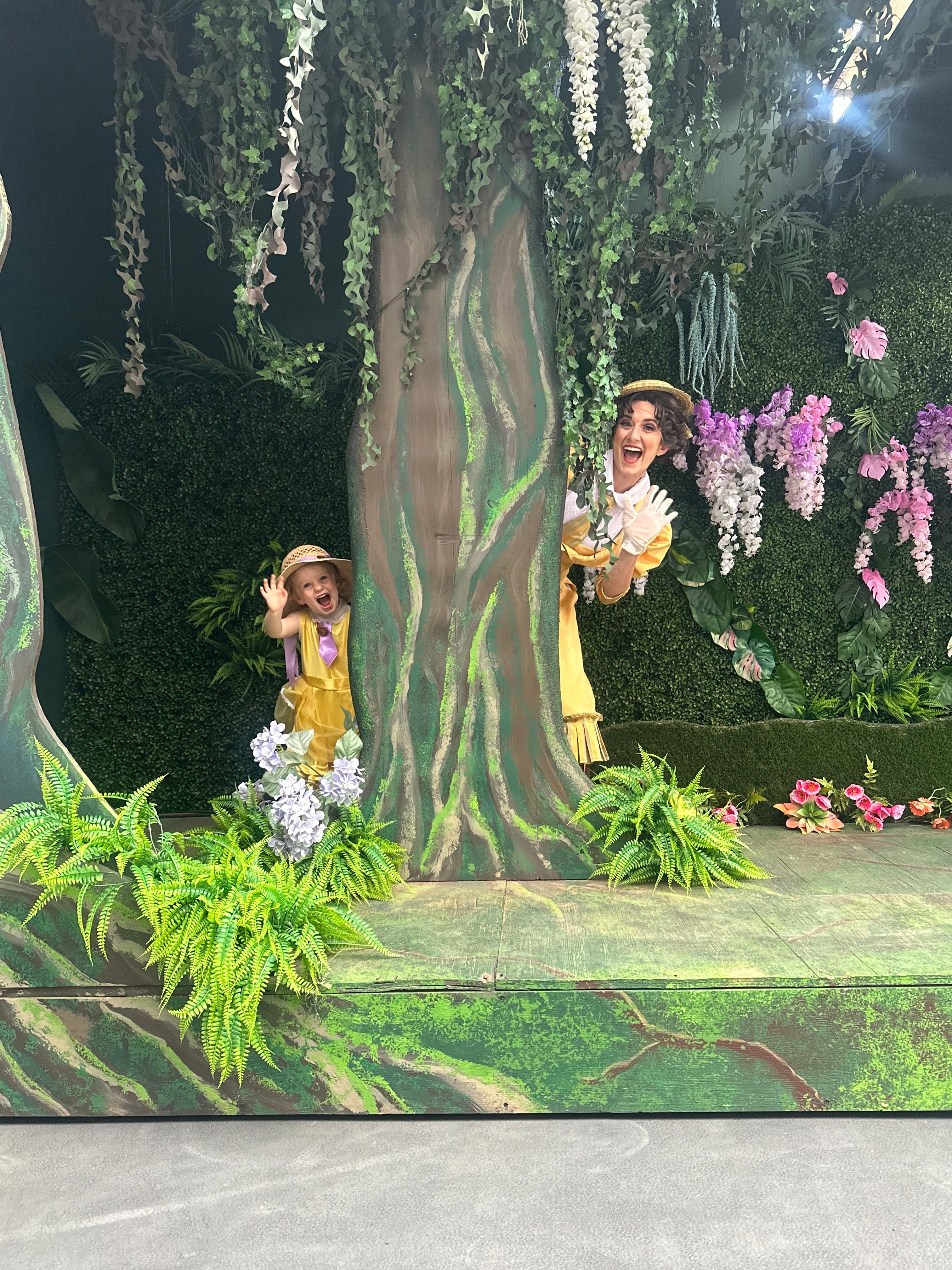 Two children in yellow outfits with flowers in a garden with trees and pink and white blossoms.