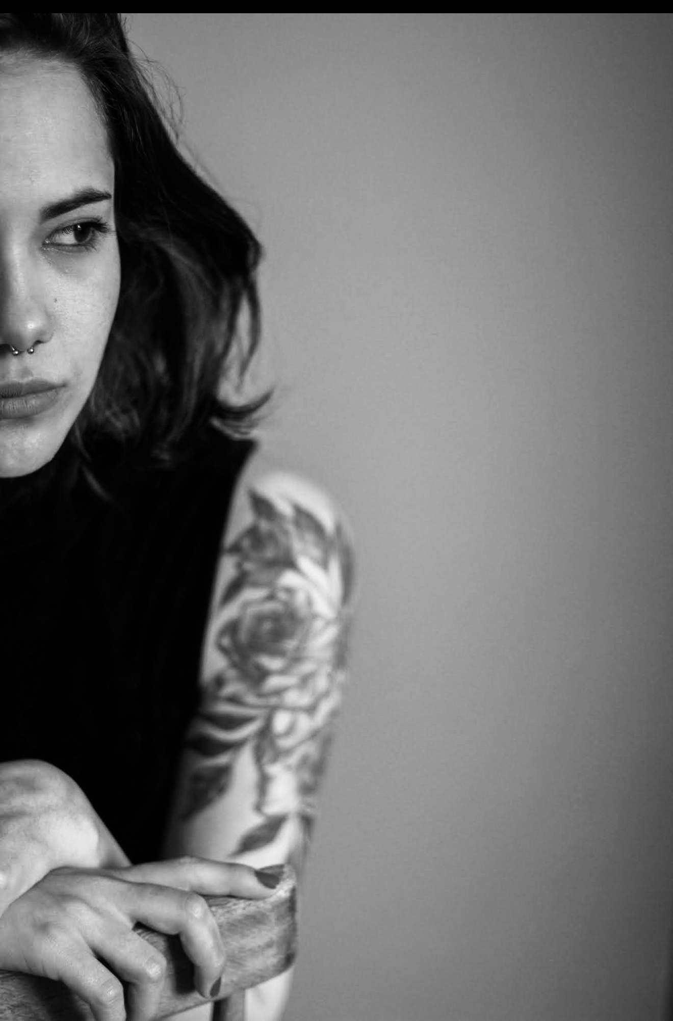Partial view of a woman with dark hair and a tattooed arm, looking to the side, in black and white.