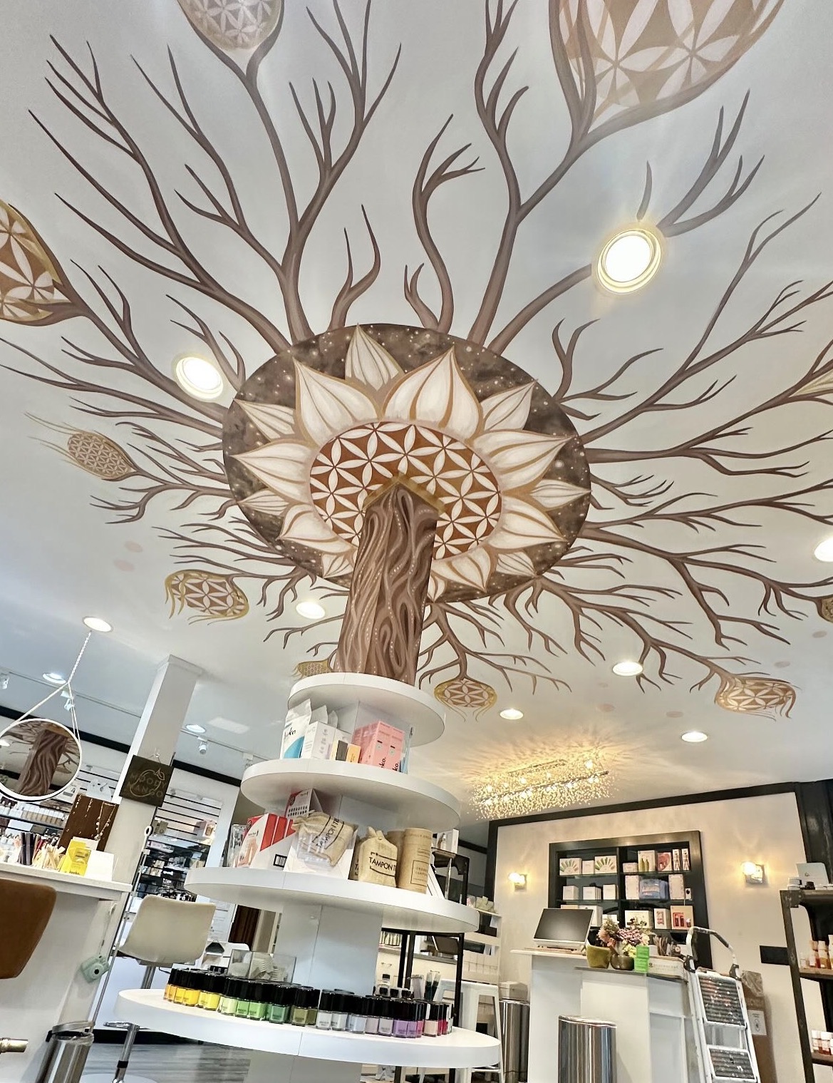 Ceiling mural of a tree with branches and leaves, featuring circular lights and intricate patterns, in a retail space.