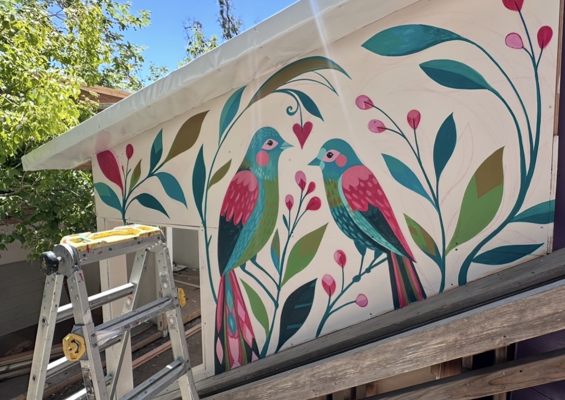 Colorful mural of two birds with pink and blue feathers among green leaves and pink berries on a wall.