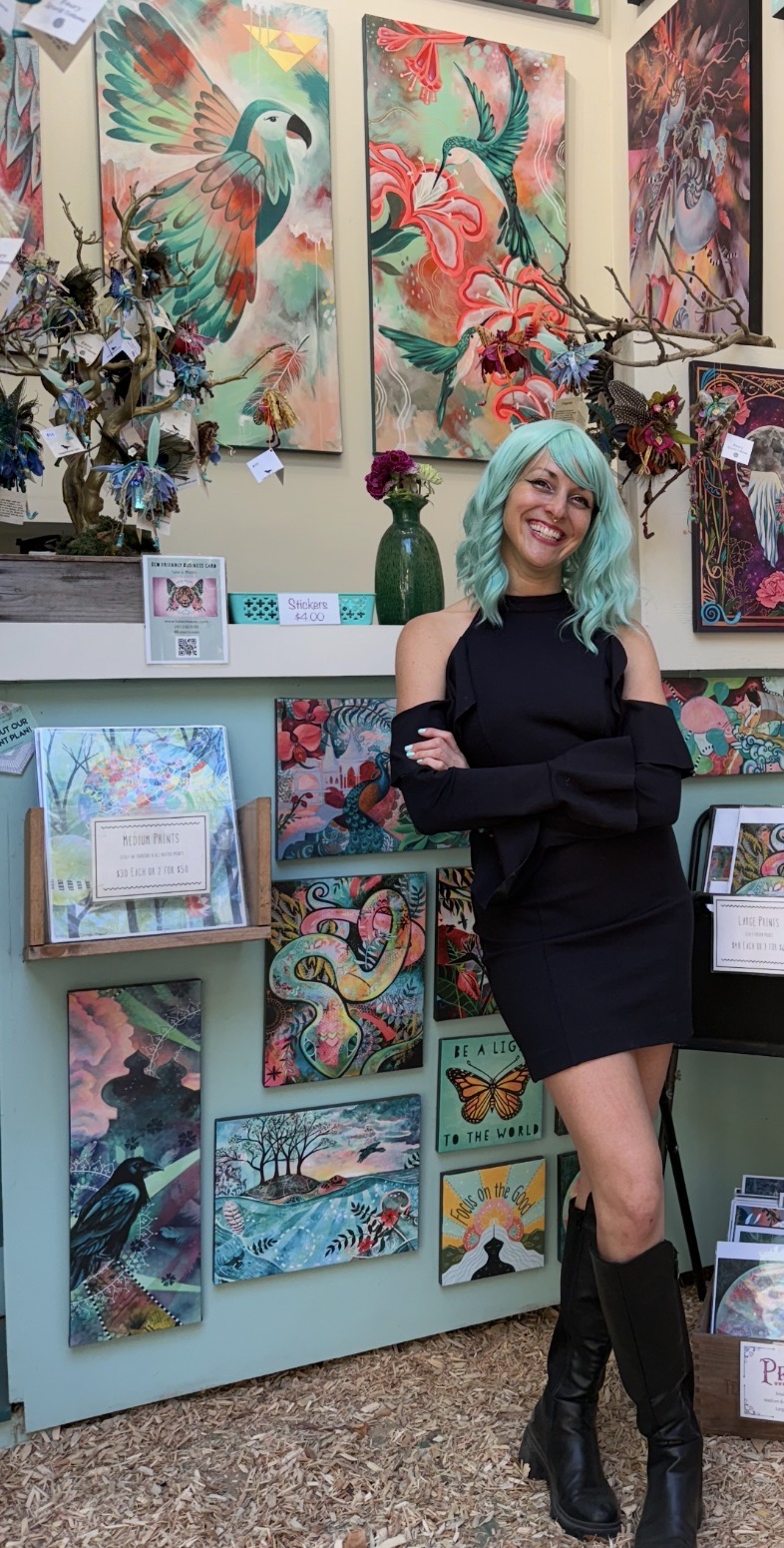 Woman with turquoise hair standing in art gallery, surrounded by colorful paintings of birds and nature, smiling with arms crossed.
