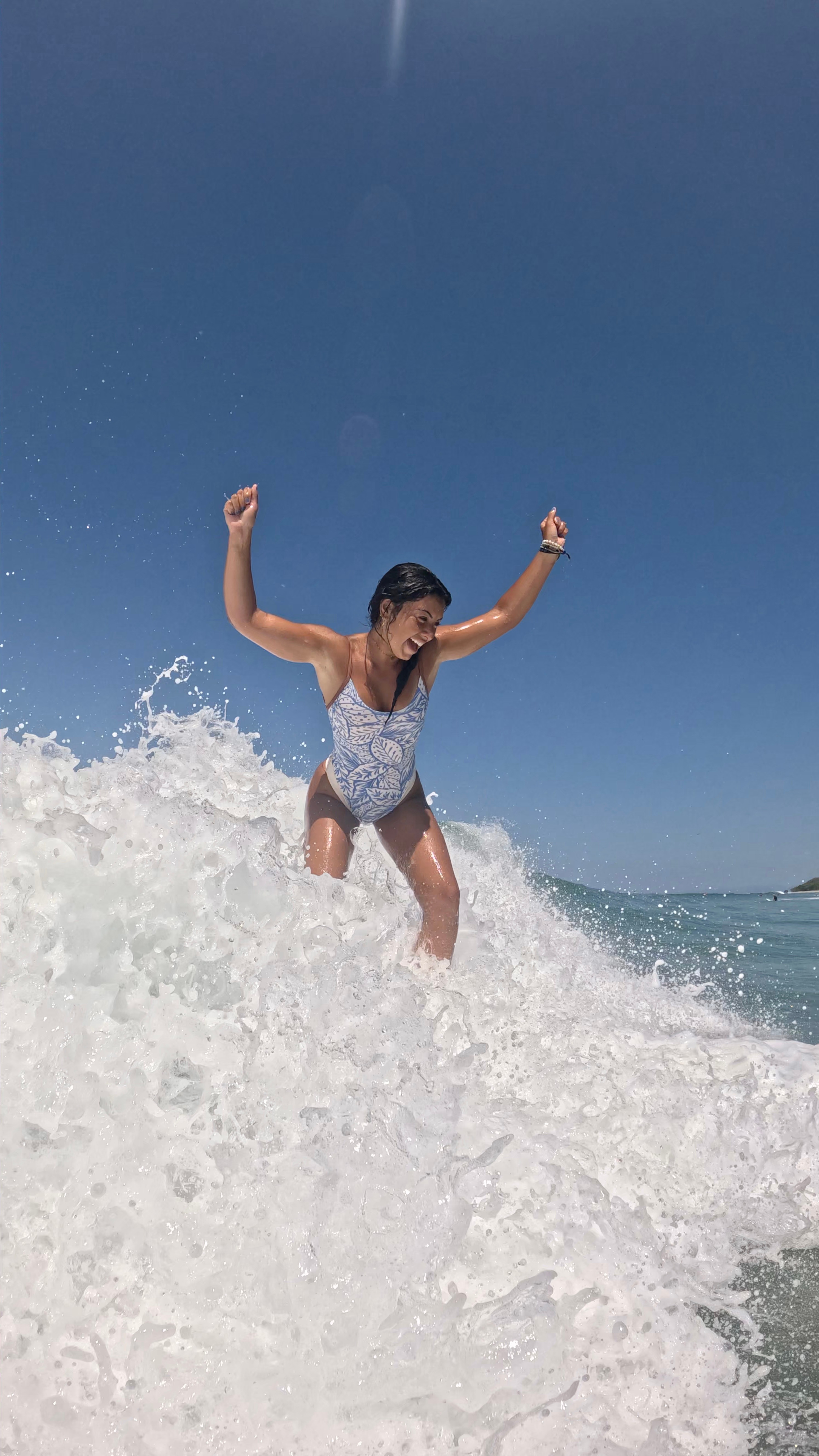 Woman in swimsuit standing on a surfboard in ocean waves under clear blue sky
