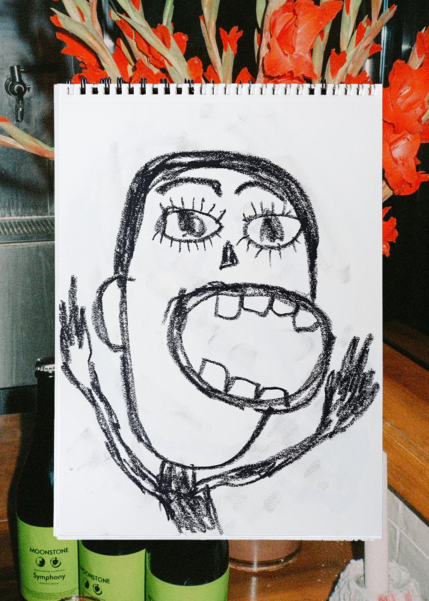 Child's drawing of a face with large open mouth, big eyes, and raised hands, on a white paper background.