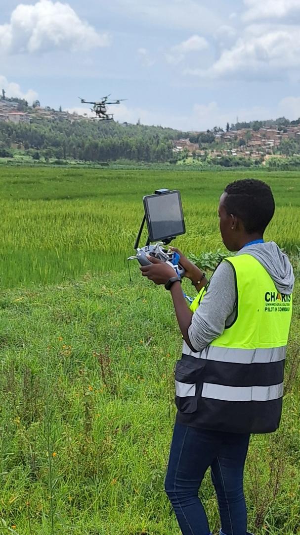 Person in a high-visibility vest controls a drone in a green field with an airplane flying overhead.