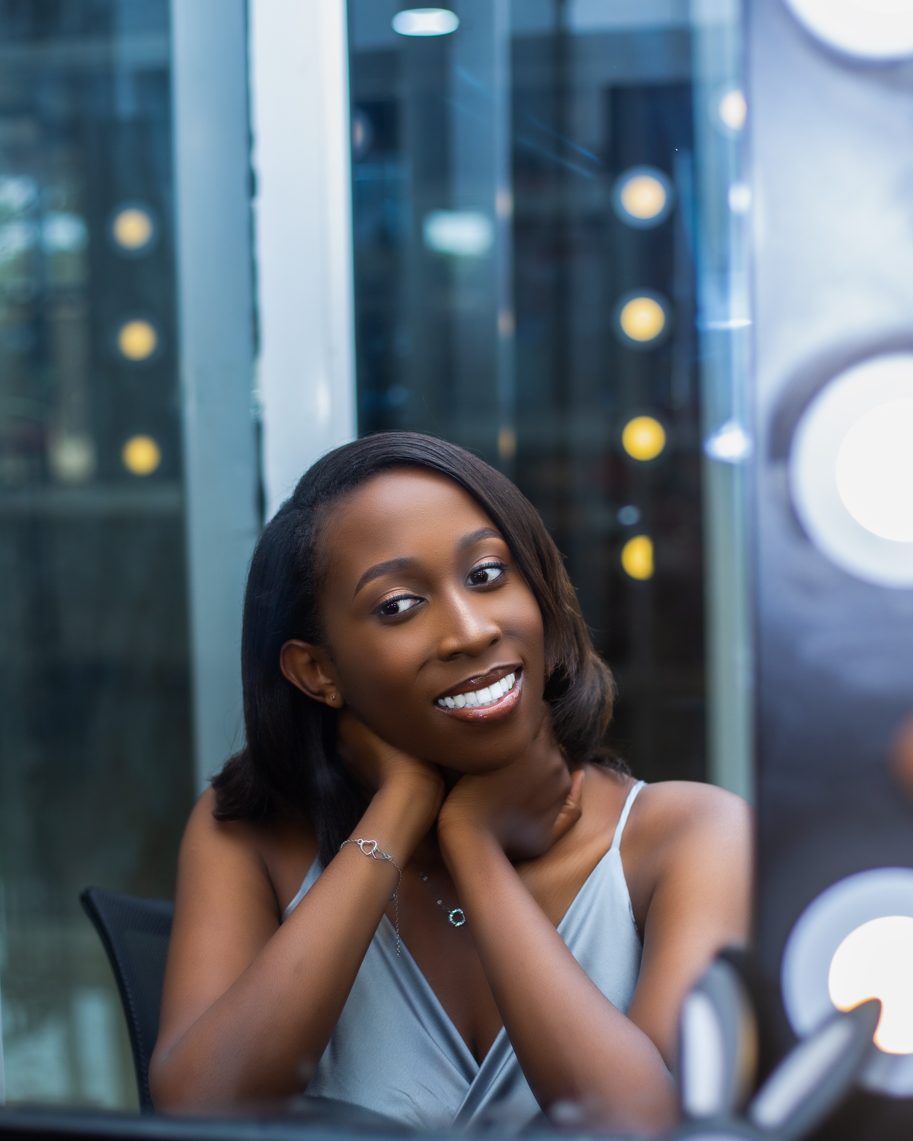 Smiling woman with shoulder-length hair, resting her chin on her hands, in a modern indoor setting.