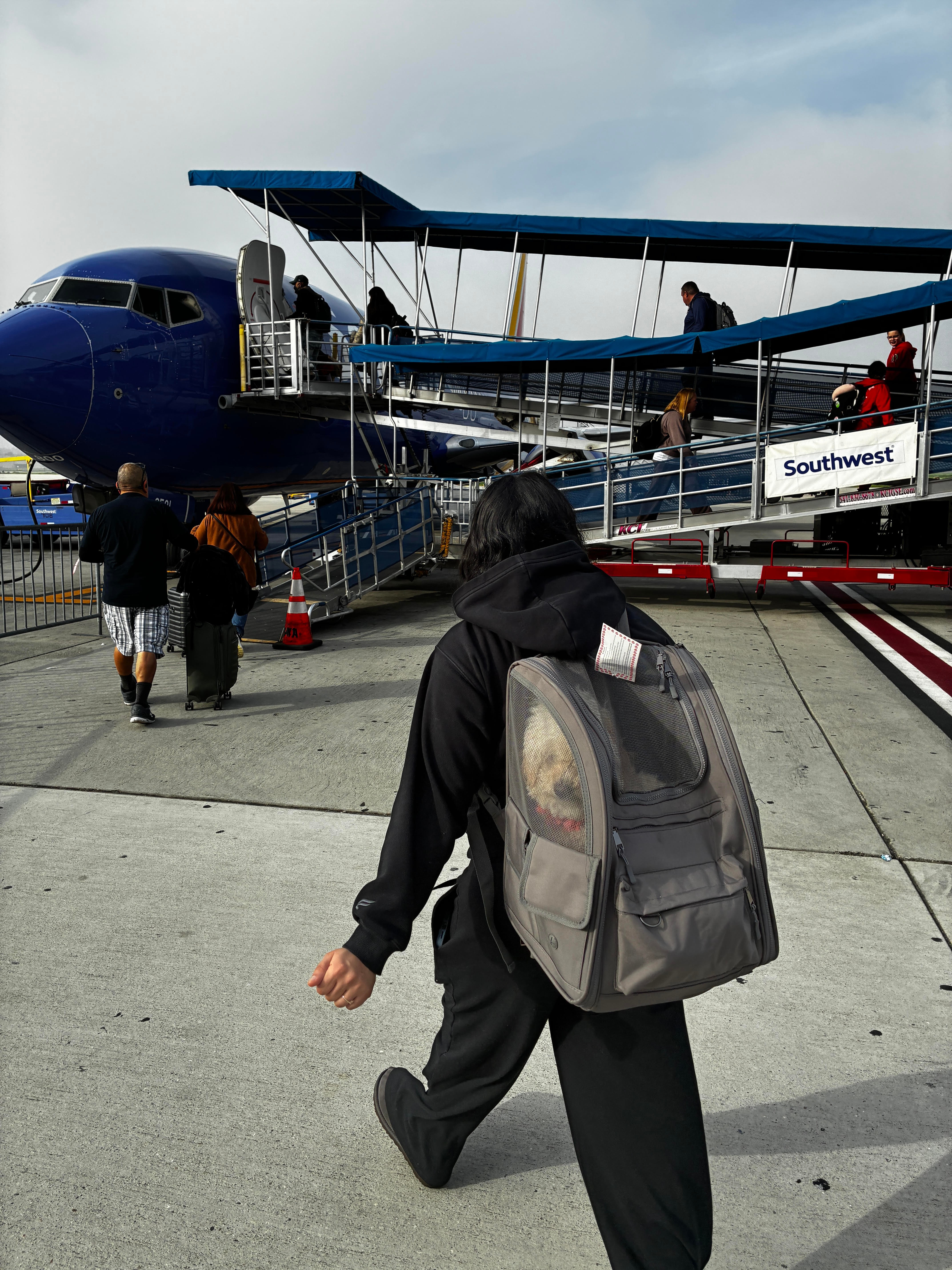 Person with backpack walking toward airplane on tarmac, with other travelers nearby and a Southwest Airlines sign visible.