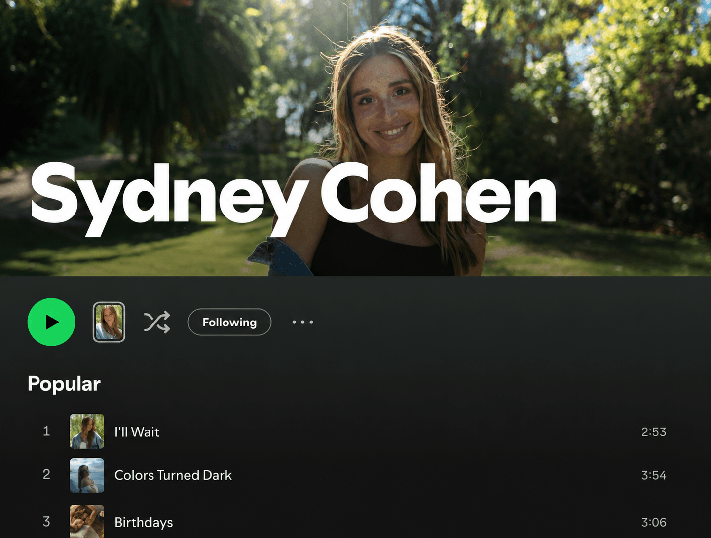 Young woman with long hair smiling outdoors in sunlight, trees in background, text overlay says 'Sydney Cohen'.