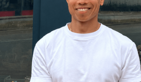 Smiling man in white t-shirt and blue cap holding a tray of assorted donuts outdoors.