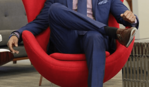 Man in a blue suit sitting in a red modern chair with a high back, in an office setting.