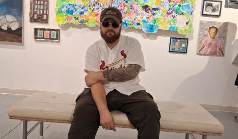Person sitting on a bench in an art gallery with colorful paintings and framed pictures on the wall behind.