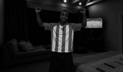 Person standing with arms raised in a room with a sofa and television, black and white image.