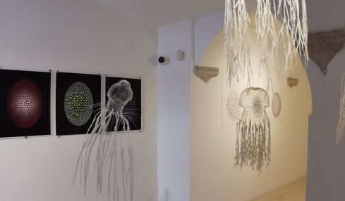 Gallery with three digital art pieces on the wall and hanging decorations resembling jellyfish or sea creatures.