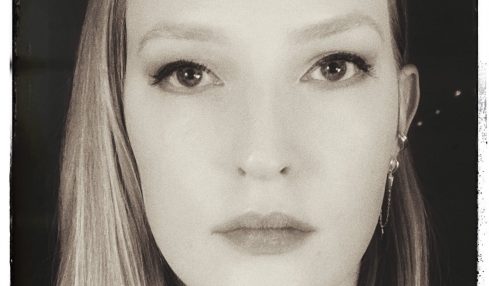 Black and white portrait of a woman with long hair, looking directly at the camera with a neutral expression.