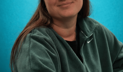 Young woman wearing a black cap and green Nike sweatshirt, smiling against a blue background.
