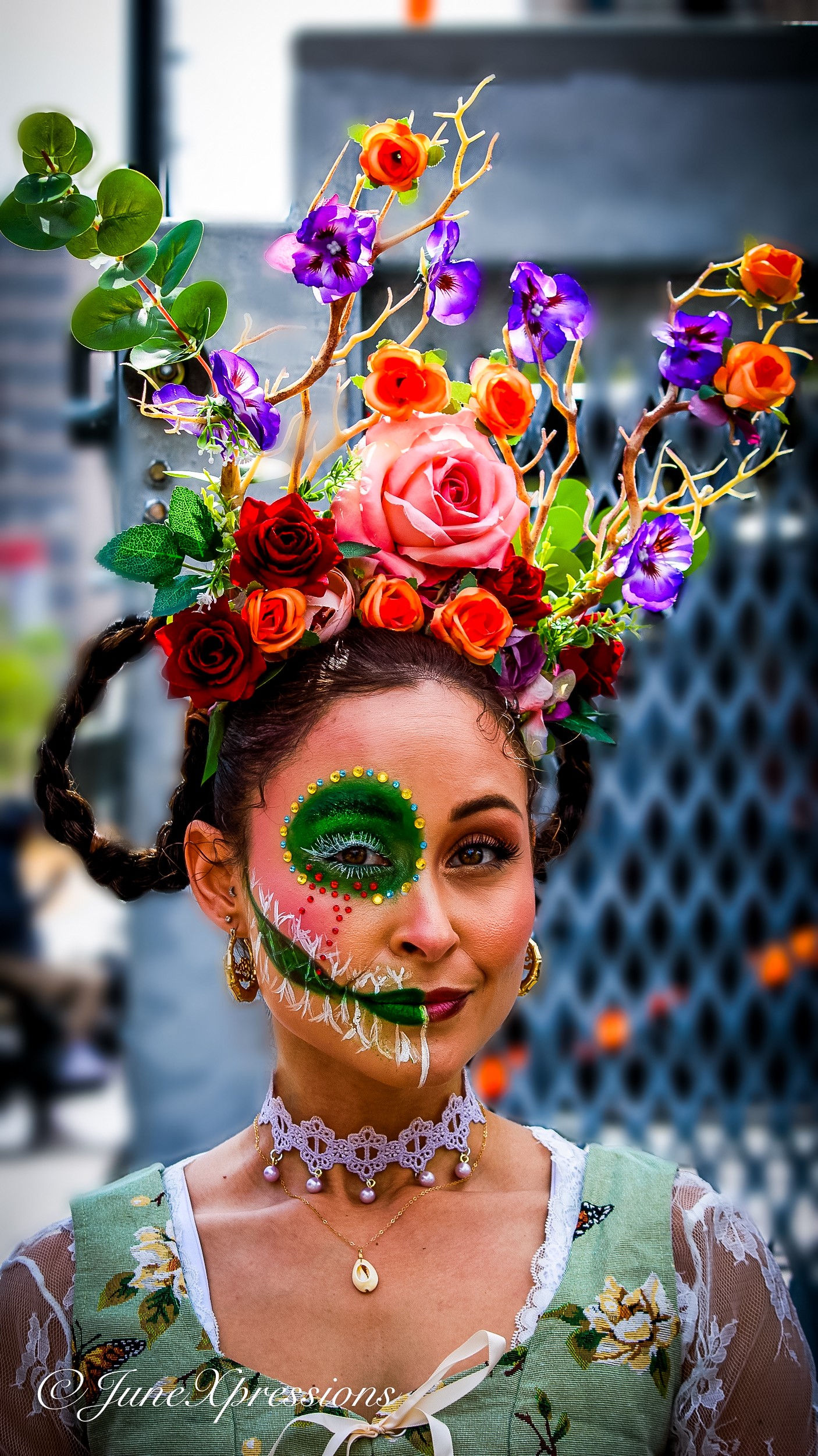 Woman with elaborate floral headpiece and face paint resembling a skull, wearing a lace top and choker necklace.